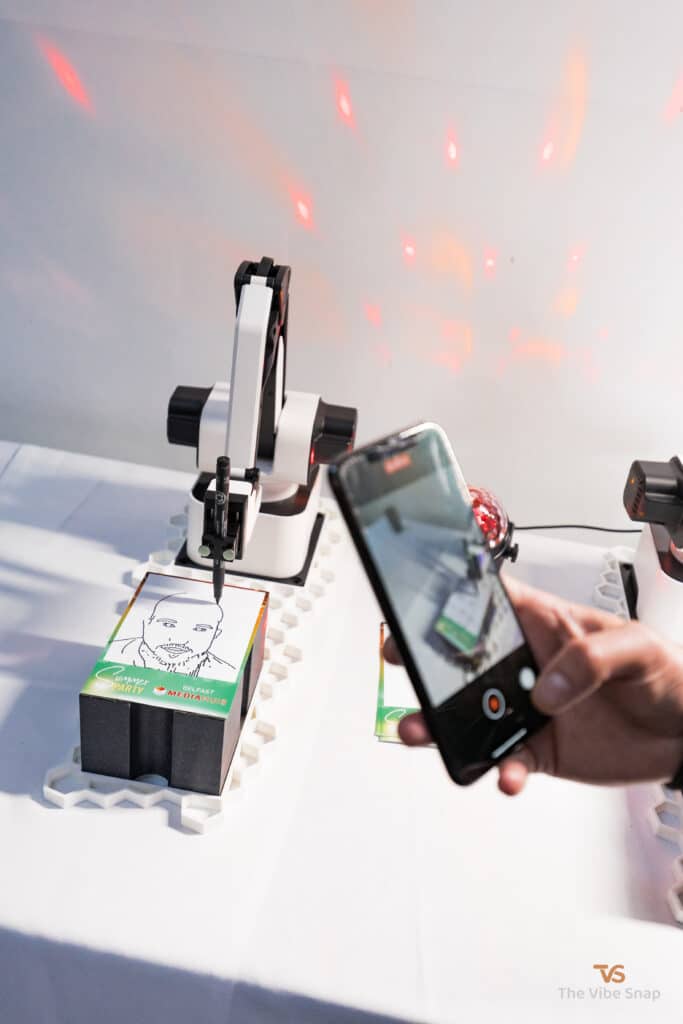 The Sketch Bot doing its thing at a party and sketching guests faces while being recorded on a mobile phone
