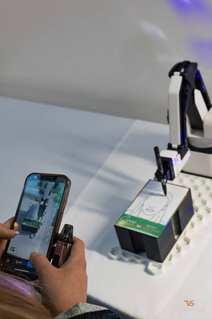 The Sketch Bot doing its thing at a party and sketching guests faces while being recorded on a mobile phone