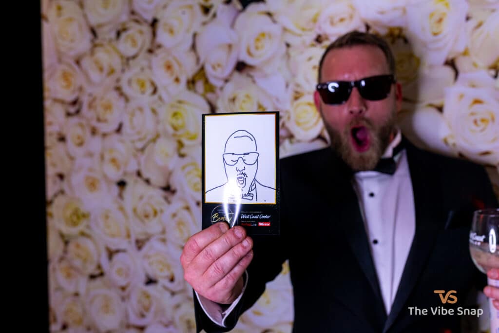 A gentleman at a party, showing a copy of his face drawn by the Sketch Bot