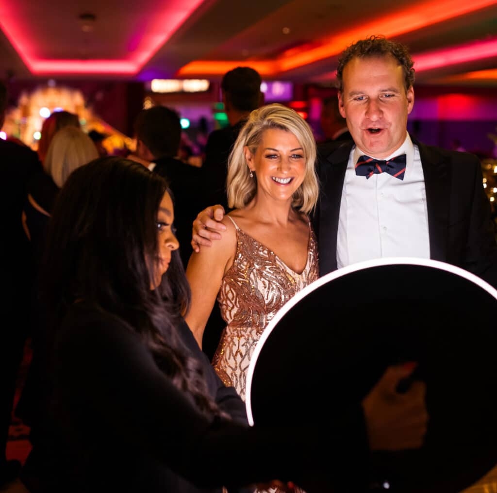 Ladies and gents at a party posing to have their photos taken on the Ipad roamer
