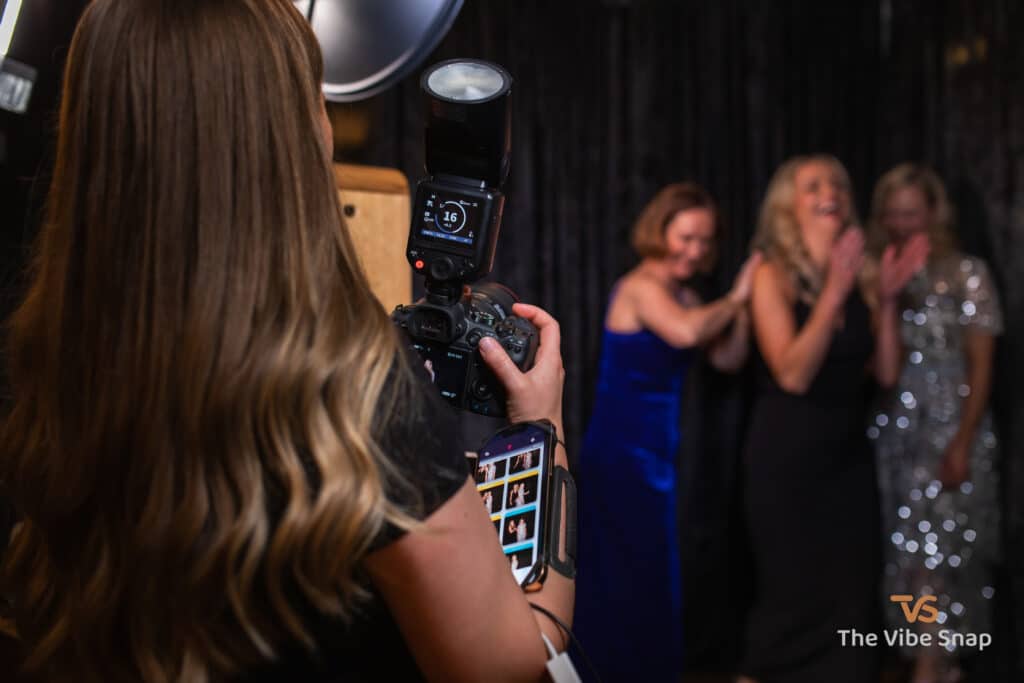 The photographer is holding a camera with an iPhone and guiding guests to strike a pose.